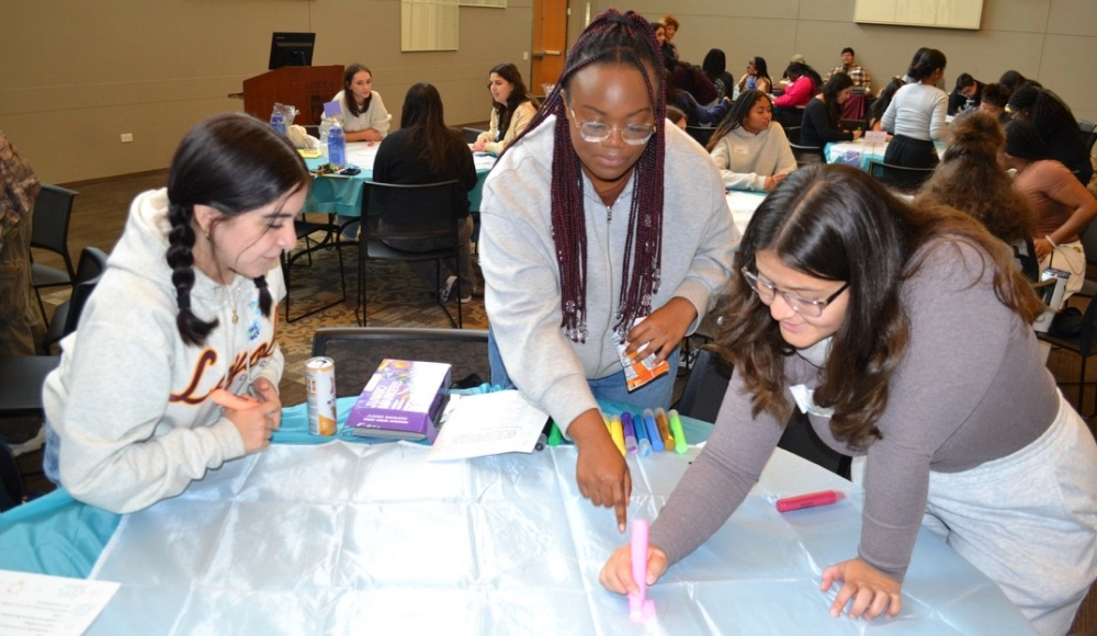 A group of three young women work together on a project at the event, focused on their drawing.